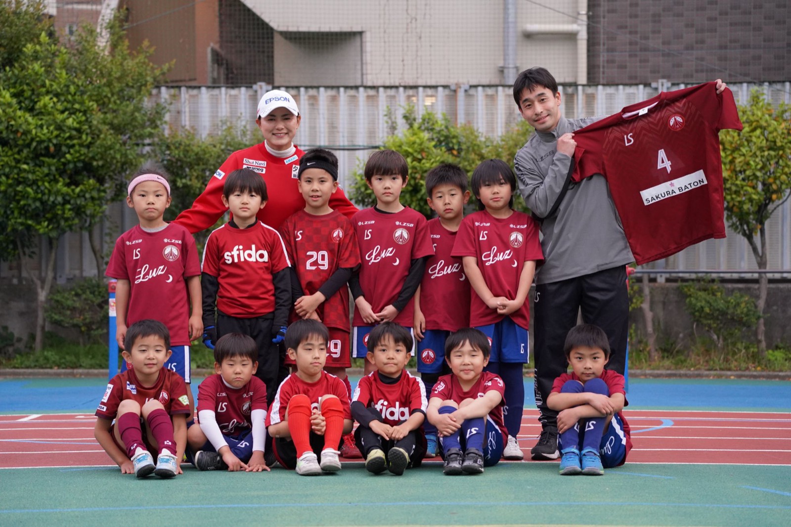 SAKURA BATONのロゴが入ったユニフォームを掲げるスタッフと、フウガドールすみだ育成カテゴリーの子どもたち、横峯さくら